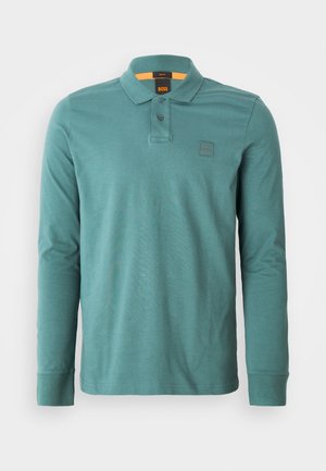 Teal spalvos medvilnės polo marškiniai ilgomis rankovėmis. Ypatybės: apykaklė, du mygtukai ir mažas logotipas ant kairės krūtinės.