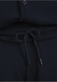 Gros plan sur un pantalon en tissu côtelé noir avec un cordon noué et un haut noir assorti boutonné.