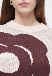 Pleteni pulover z vinsko rdečim in svetlo rožnatim cvetličnim vzorcem, s širokim okroglim ovratnikom in mehko teksturo ter rahlo sproščenim prileganjem.