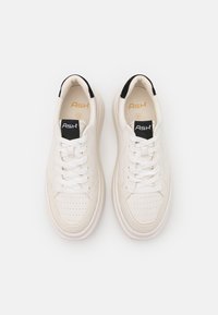 Vita idrottsskor i vitt med perforerat ovandel, platta snören och en kontrasterande svart hälflik. Har guldtext på tungan.