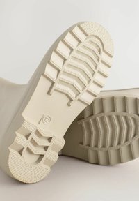 Suole di stivali in gomma beige con un profondo motivo di battistrada, caratterizzate da punti sollevati per una migliore aderenza e un distintivo contrassegno di taglia "12".