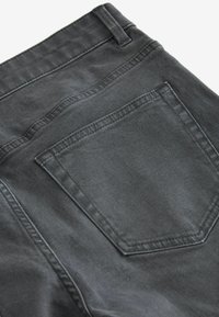 Gros plan sur un jean en denim gris foncé montrant la poche arrière, la ceinture et la boucle de ceinture avec des détails de couture visibles.
