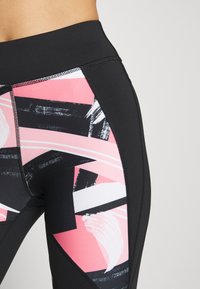 Højtaljede, sorte leggings med dristige pink, sorte og hvide abstrakte mønstre samt teksturerede paneler på siderne. Glat stoffinish.