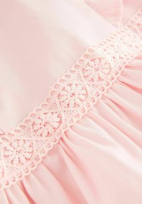 Robe rose pâle ornée d'une broderie florale délicate le long de l'encolure et d'un design de tissu texturé froncé.