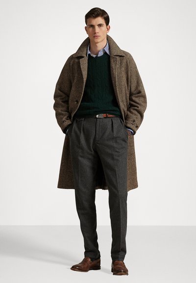 Manteau en laine à chevrons, pull en maille torsadée vert, chemise rayée, pantalon plissé gris, chaussures en cuir marron et ceinture en cuir.