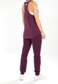 Lilla atletisk tanktop med racerback-design, parret med matchende lilla joggingbukser; begge lavet af glat stof og tætsiddende pasform.