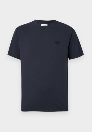 Camiseta azul marino de manga corta con cuello redondo, con un pequeño logo en relieve en el pecho izquierdo y una etiqueta de marca blanca dentro del cuello.