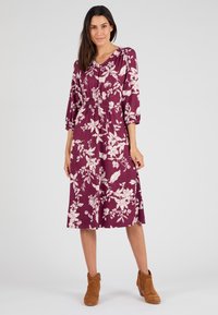 Robe bordeaux avec un motif floral, dotée de manches 3/4, d'un décolleté en V et d'une taille élastique. Associée à des bottes cheville en daim marron.