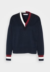 Granatowy sweter z dzianiny z dekoltem w kształcie litery V, ozdobiony akcentami w trzech kolorach: białym, czerwonym i granatowym. Ściągacze na mankietach i u dołu. Długie rękawy.