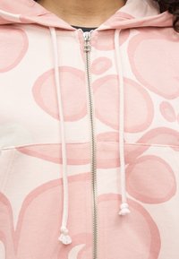 Ανοιχτό ροζ φούτερ με φερμουάρ και λευκά κορδόνια, με μεγάλα, ακανόνιστα, παλ ροζ σχέδια. Μαλακή υφή υφάσματος και μεταλλική λεπτομέρεια στο φερμουάρ.