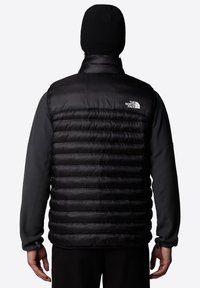 Zwarte puffy gilet met een horizontaal quilted ontwerp, grijze fleecemouwen en een hoge kraag. Inclusief een logo aan de bovenkant aan de rechterzijde.