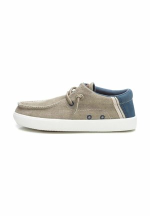 Zapatillas de lona beige con suela de goma blanca, talón azul oscuro, rayas laterales en contraste y costuras decorativas en la parte superior.