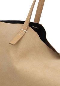 Bolso de ante beige con forro negro, que presenta una textura suave, asas delgadas y un diseño minimalista. Sin hardware visible ni adornos.