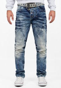 Jeans en denim bleu avec une finition décolorée et texturée. Dotés d'une braguette zippée, de plusieurs boutons et d'une coupe slim avec des détails sur les panneaux de genoux.