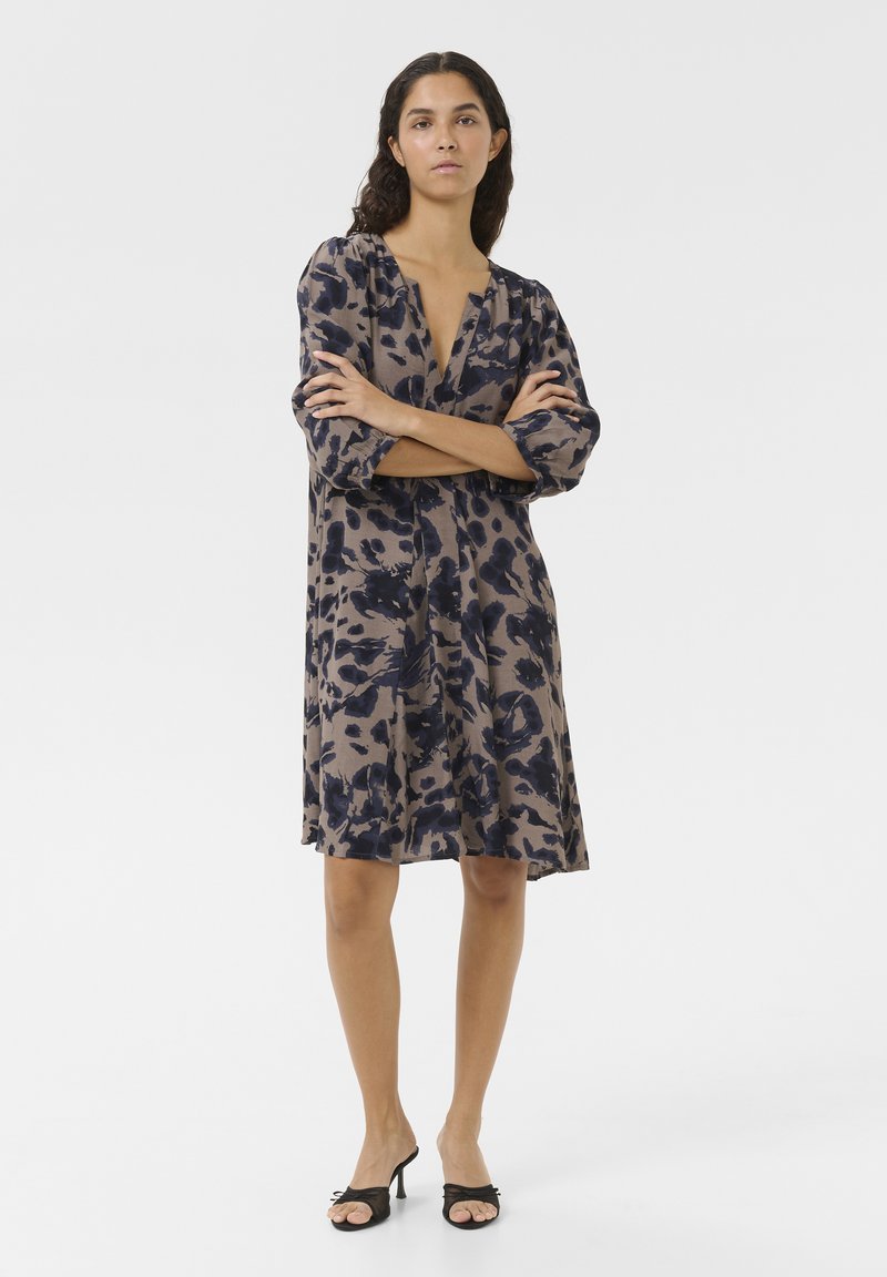 Robe imprimée à coupe ample, présentant une base beige avec des motifs floraux bleu foncé, un décolleté en V profond et des manches bouffantes trois-quarts.