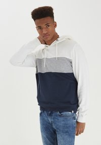 Hoodie s dizajnom u boji u bijeloj, sivoj i mornarskoj plavoj. Izrađen od mekog materijala s prednjim džepom i špagama na kapuljači.