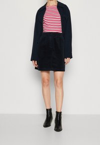 Falda de pana azul marino con cintura elástica, combinada con una camisa de rayas rojas y blancas y botines negros. Texturas suaves y diseño ajustado.