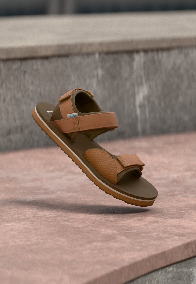 Καφέ σανδάλι με δύο ρυθμιζόμενους ιμάντες Velcro, υφασμάτινο συνθετικό επάνω μέρος με υφή, μαλακό πέλμα και ελαστική σόλα με ραβδώσεις.