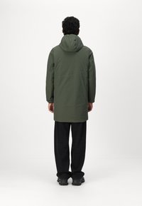 Parka à capuche verte au design minimaliste, avec une coupe droite et des manches longues. Le tissu semble lisse avec une finition mate.