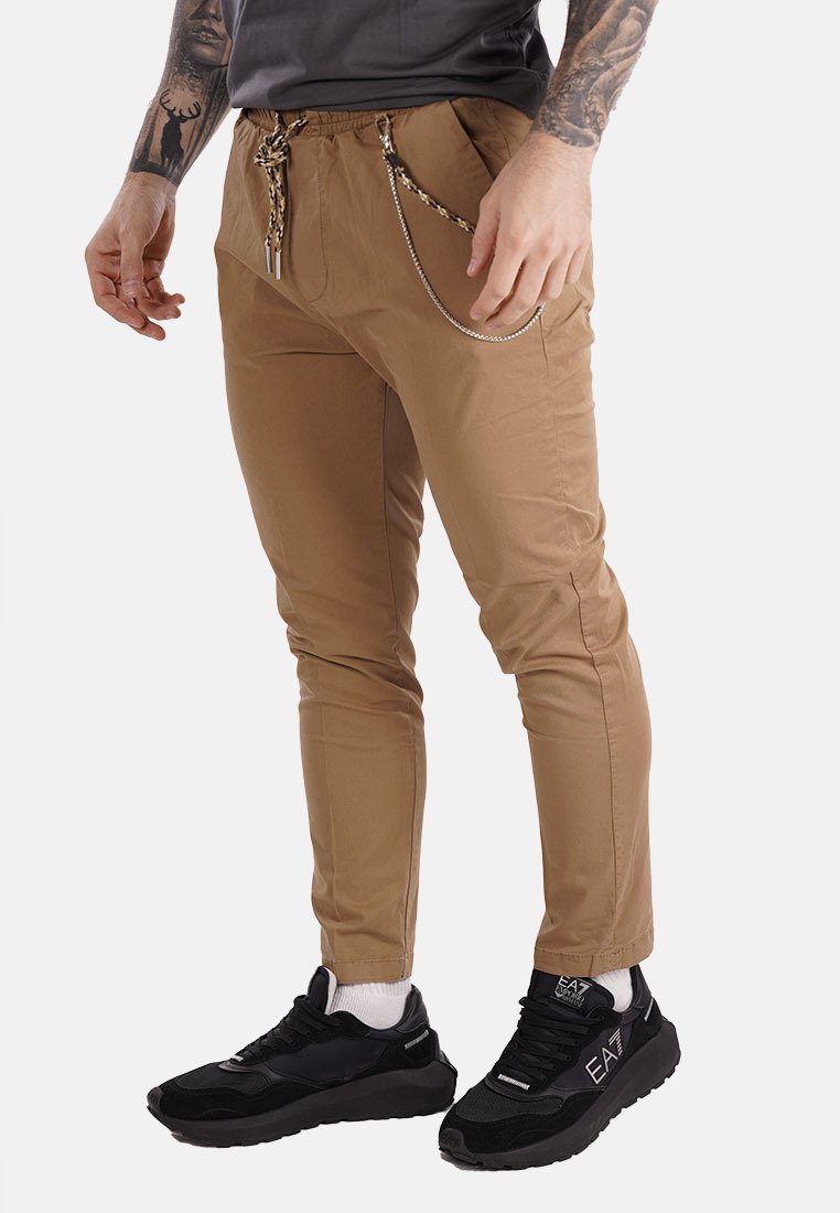 Pantalones beis de corte ajustado, con bolsillos laterales y un detalle de cadenas. Combinados con zapatillas deportivas negras y calcetines blancos hasta el tobillo.
