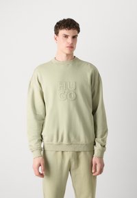 Világos zöld pamutsweatshirt ribbelt mandzsettákkal és aljjal, az elején dombornyomott "HUGO" logóval. Puha tapintás és laza szabás.