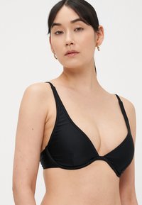 Μπικίνι τοπ με μαύρο τριγωνικό σχήμα, λεπτές ρυθμιζόμενες τιράντες και ομαλή υφή. Διαθέτει βαθύ ντεκολτέ και άνετη, χωρίς ραφές, σχεδίαση.