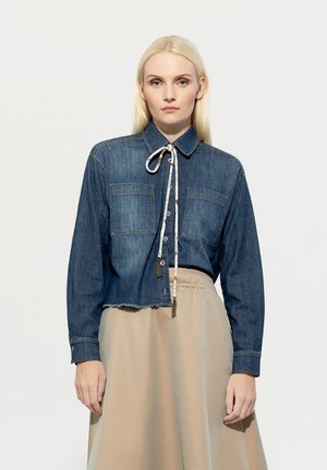 Denim shirt with a cropped design, two chest pockets, long sleeves, and a tied neck detail. Features a frayed hem in dark blue.