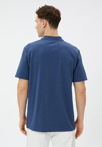 Mørkeblå kortærmet polo-shirt med en subtil tekstur, klassisk krave og lige kant, vist fra ryggen.
