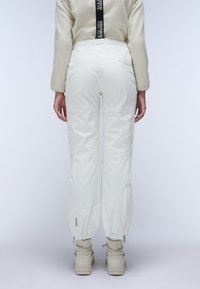 White, waterproof pants with a drawstring ankle, zip closures, and a logo detail on the left thigh, paired with light-colored footwear.