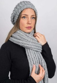 Šedá pletená čepice a šála, s výraznou, texturovanou vazbou. Čepice má volný střih, zatímco šála je široká a jemně visí.