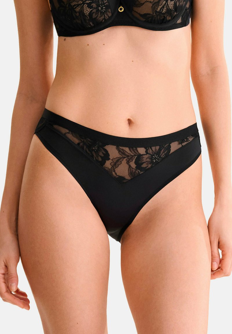 Ensemble de lingerie en dentelle noire et tissu avec des motifs floraux, des panneaux en maille et une taille solide. La coupe haute met en valeur la forme des jambes.