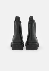 Botas negras hasta el tobillo con un acabado de cuero suave, paneles laterales elásticos y una suela de goma gruesa con un acabado texturizado.