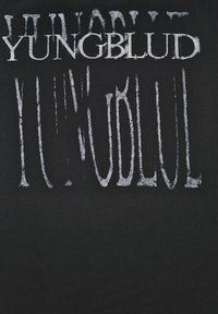 Svart t-shirt med stor, slitna vit text som läser "YUNGBLUD" i olika storlekar och riktningar, vilket skapar en lager-effekt.