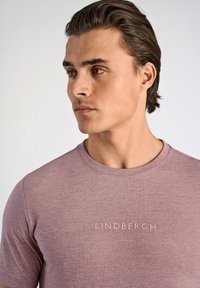 Kortärmad lila t-shirt gjord av mjukt tyg, med rund hals och präglad "LINDNERGH"-logotyp i en ljusare nyans.
