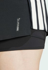 Crne atletske kratke hlače od teksturiranog materijala, s bijelim "CLIMACOOL" logotipom i crno-bijelim prugastim akcentima sa strane.