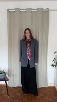 Oversized grå blazer over en beige topp, kombinert med vide svarte bukser. Et langt rosa skjerf med mønster fullfører antrekket.