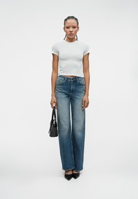 Bela prilegajoča majica s kratkimi rokavi v kombinaciji z modrimi širokimi hlačami. Črna torba z tankimi trakovi. Model nosi črne čevlje s koničastim nosom. Minimalistična zasnova.