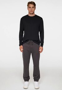 Czarna koszula z długim rękawem w połączeniu z szarymi dresami. Dresy mają elastyczny pas z troczkami. Całość dopełniają białe trampki.