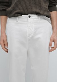 Witte katoenen broeken met een recht gesneden ontwerp, met een zwarte knoopsluiting en zijzakken. Textuur ribgebreide trui zichtbaar erboven.
