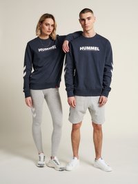 Felpa navy con logo "HUMMEL", accenti a zigzag bianchi; leggings e pantaloni corti grigi; tessuto misto; abbigliamento sportivo casual; sneakers bianche.