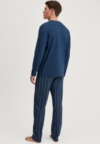 Marineblauw longsleeve shirt met ronde hals, gecombineerd met gestreepte pyjamabroek met een ruitpatroon in blauw, accentueert met bruine lijnen.