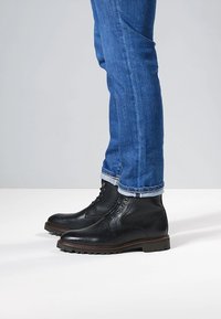 Schwarze Leder-Stiefeletten mit strukturierter Oberfläche, rundem Zehenbereich und brauner Gummisohle, kombiniert mit hochgekrempelten blauen Jeans.