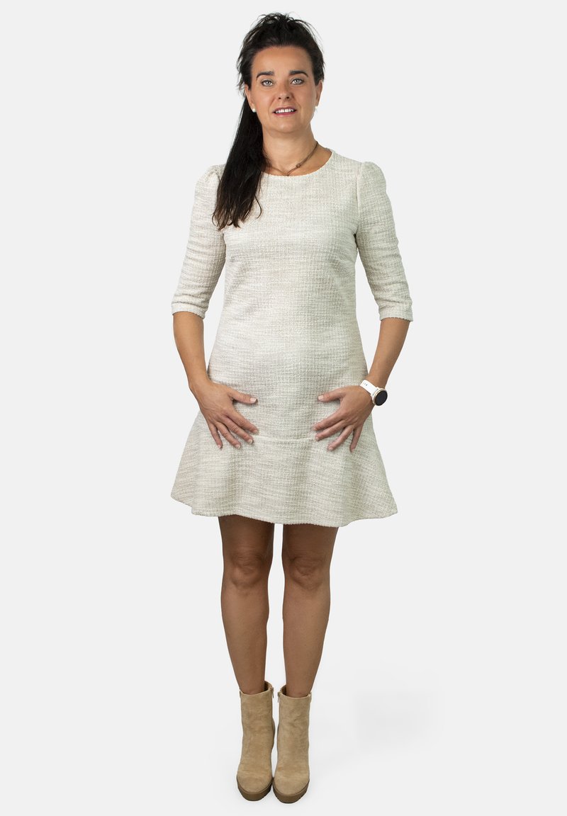 Vestido beige texturizado con mangas tres cuartos y una falda acampanada, combinado con botines de tobillo marrón claro. Diseño sencillo sin patrones.