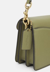 Torebka z oliwkowej zielonej skóry o fakturze z detalami ze złotego metalu, z metką logo Coach i łańcuszkiem przy mocowaniu paska.