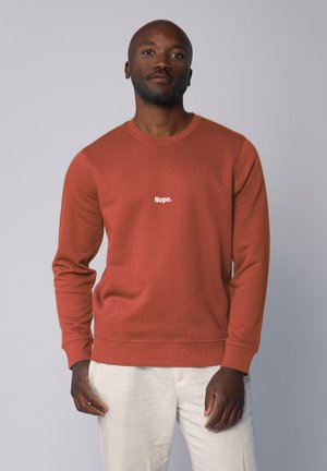 Baksteenrode sweatshirt met ronde hals, lange mouwen en witte tekst "Nope." op de borst. Gemaakt van zachte stof met een gladde textuur.