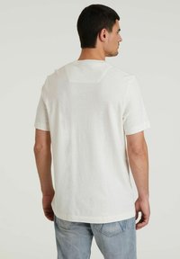 T-shirt bianco a maniche corte in misto cotone, con scollatura rotonda e design semplice, che presenta un piccolo logo sul retro.