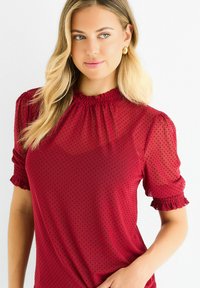 Red sheer blouse with dotted pattern, gathered neckline, and puffed short sleeves with ruffled cuffs. Soft texture and light weight.