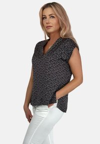 Czarna bluzka z krótkim rękawem, w białe plamki, z dekoltem w serek i luźnym krojem, zestawiona z białymi dżinsami.