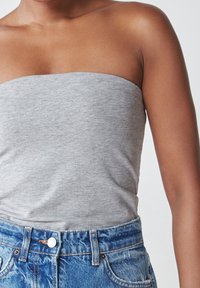 Grå strapless top lavet af blødt stof, parret med blå denim højtaljede shorts med frontlommer og knaplukning.