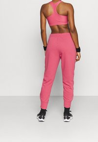 Rosa sportliche Jogginghosen mit entspanntem Schnitt und schmal zulaufendem Knöchel. Kombiniert mit einem passenden Sport-BH. Schwarze Handgelenkbänder und Sportschuhe sichtbar.